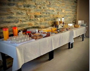 Una mesa de buffet con distintos alimentos y bebidas, frente a una pared de piedra.