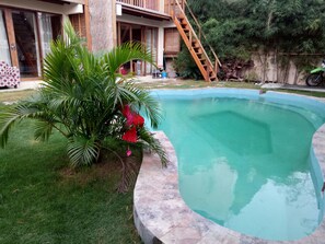 A swimming pool with a wooden staircase leading to a house. - Bamboo bungalow (Kuta)