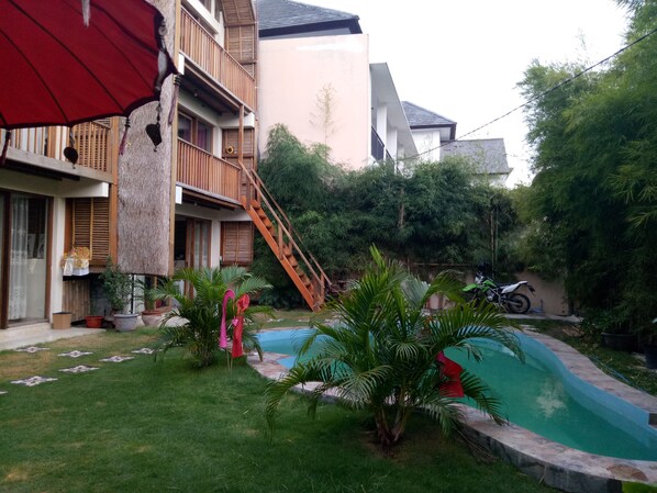 A residential area with a swimming pool, a staircase leading to a balcony, and various potted plants. - Bamboo bungalow (Kuta)