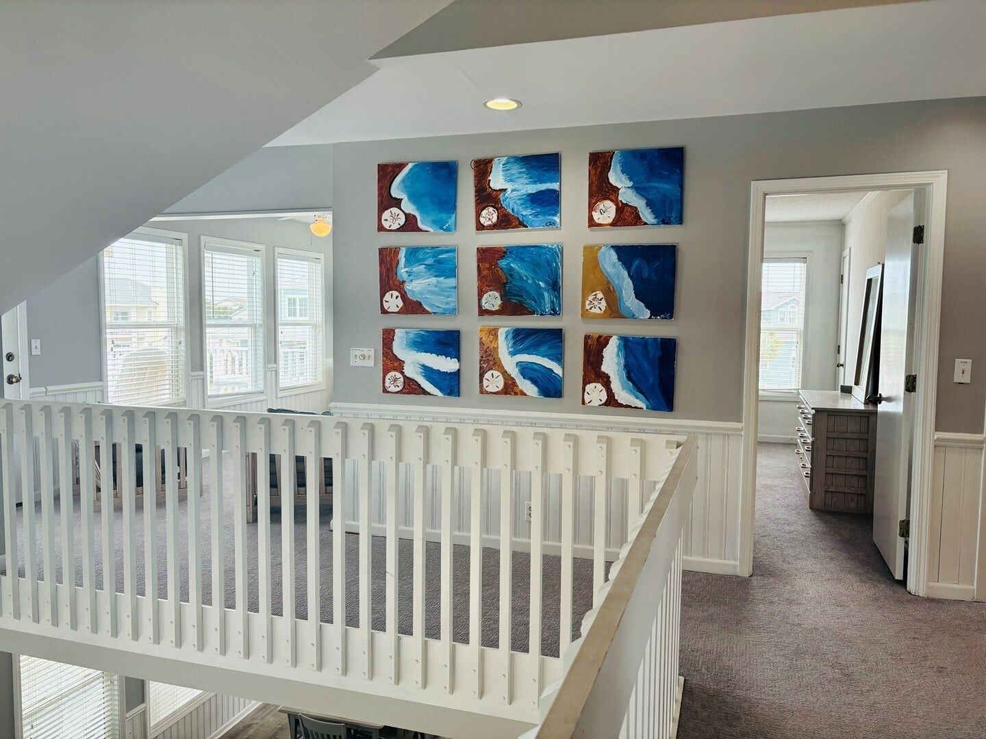 A room with a white railing, a view of the outside, and a wall with multiple paintings.