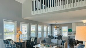 A spacious living room with a high ceiling, large windows, a dining area, and a kitchen. - Long Grass 5 Bedroom Home by RedAwning (Supply)
