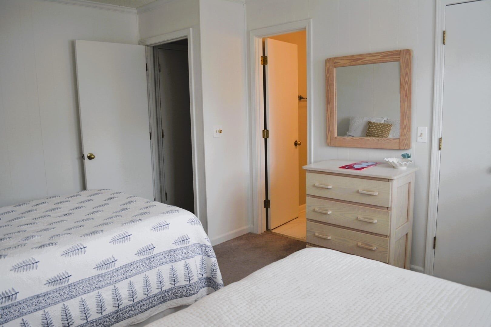 Une chambre à coucher comprenant un lit, une commode, un miroir et une porte donnant accès à une salle de bain.