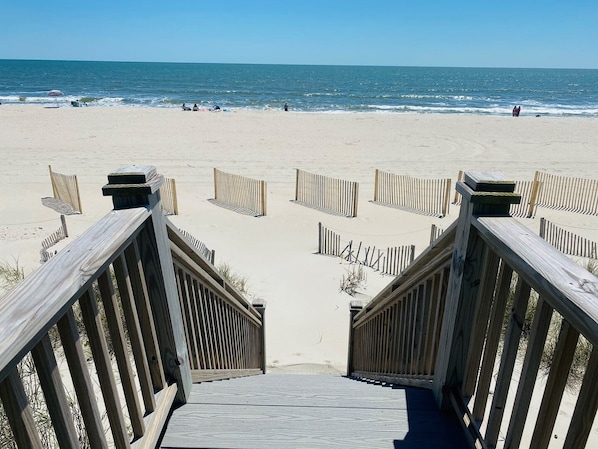 A wooden boardwalk leading to a sandy beach with a clear view of the ocean.