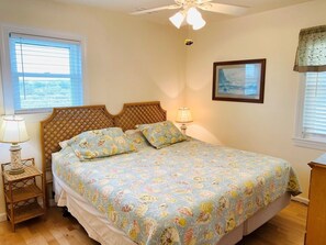A bedroom with a bed, a bedside lamp, a ceiling fan, and a window with blinds.