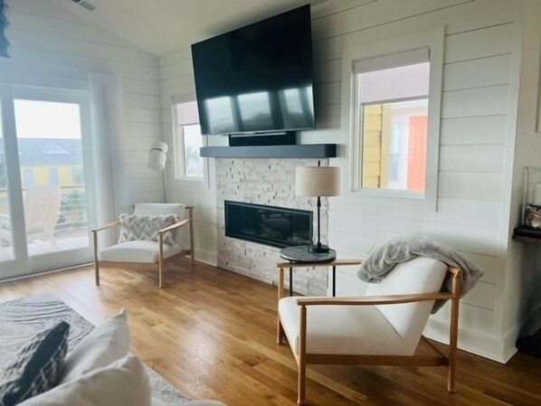 Una sala de estar moderna con chimenea, un televisor de pantalla plana montado encima y dos sillones blancos.