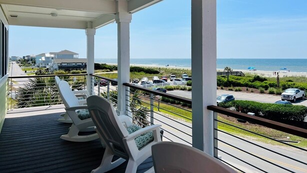 A covered balcony with white chairs, a view of the beach, and parked cars. - The Rainbow Connection 4 Bedroom Home by RedAwning (Supply)
