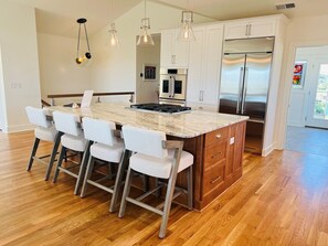 A modern kitchen with a central island, bar stools, stainless steel appliances, and pendant lighting. - The Rainbow Connection 4 Bedroom Home by RedAwning (Supply)