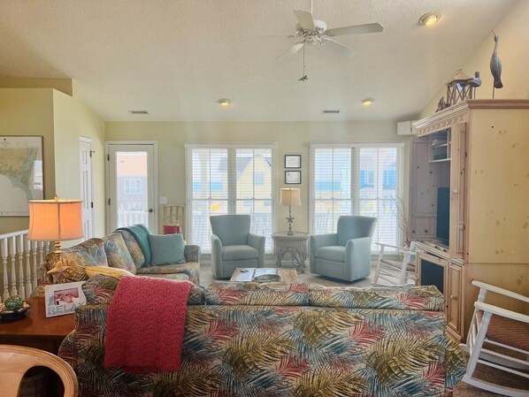 Un salon avec un canapé à motifs, deux fauteuils, un ventilateur de plafond et un téléviseur.