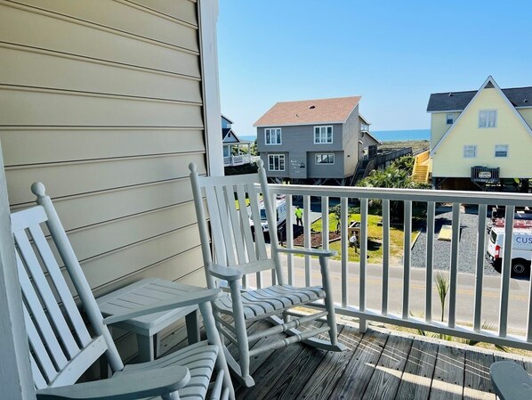 A wooden deck with white chairs, a railing, and a view of houses and a road.