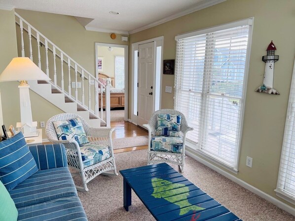 Un salon avec un escalier, deux fauteuils en osier, un canapé bleu et une table basse.