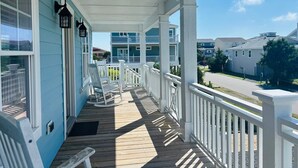 Une véranda couverte avec des balustrades blanches et une terrasse en bois, donnant sur un quartier résidentiel avec des maisons.