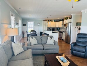 A living room with a grey sofa, a black leather chair, a wooden coffee table, and a kitchen in the background. - Blue Sunset 4 Bedroom Home by RedAwning (Supply)