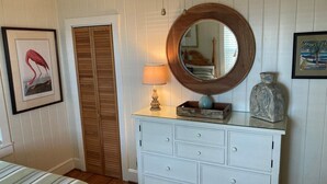 A room with a bed, a dresser with drawers, a mirror, a lamp, and two framed pictures on the wall.