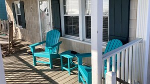 A covered porch with wooden flooring, two turquoise Adirondack chairs, and a white railing.