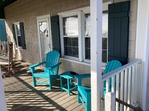 Een overdekt terras met houten vloer, twee turkozen Adirondack stoelen en een witte balustrade.