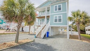 A two-story beachfront house with a balcony, a staircase, and a small porch area. - Life's A Beach 4 Bedroom Home by RedAwning (Supply)