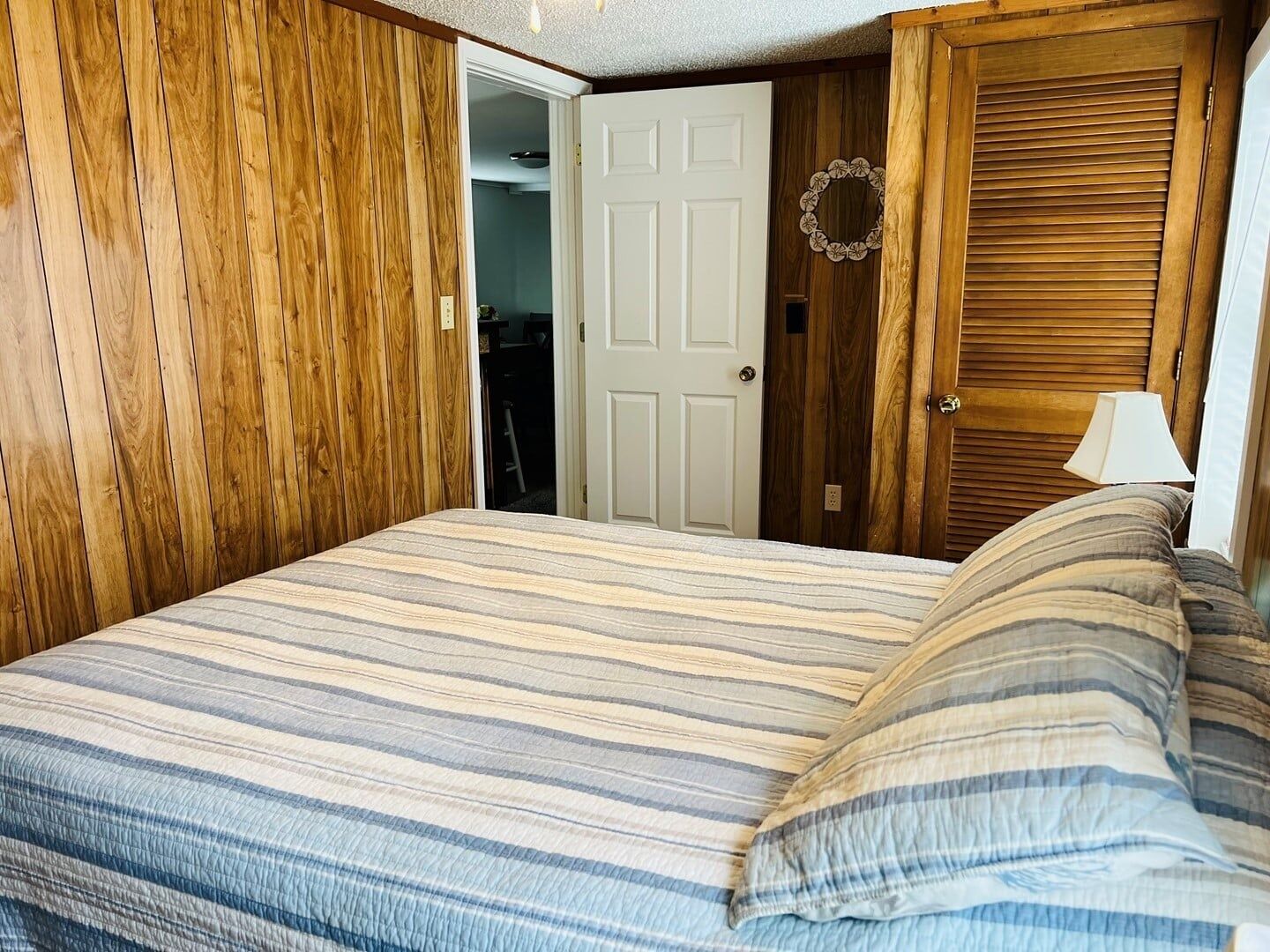 Un dormitorio con una cama, paredes de madera, una puerta blanca y una lámpara.