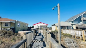 A wooden boardwalk leading to a building with a red roof, surrounded by wooden fences and vegetation.