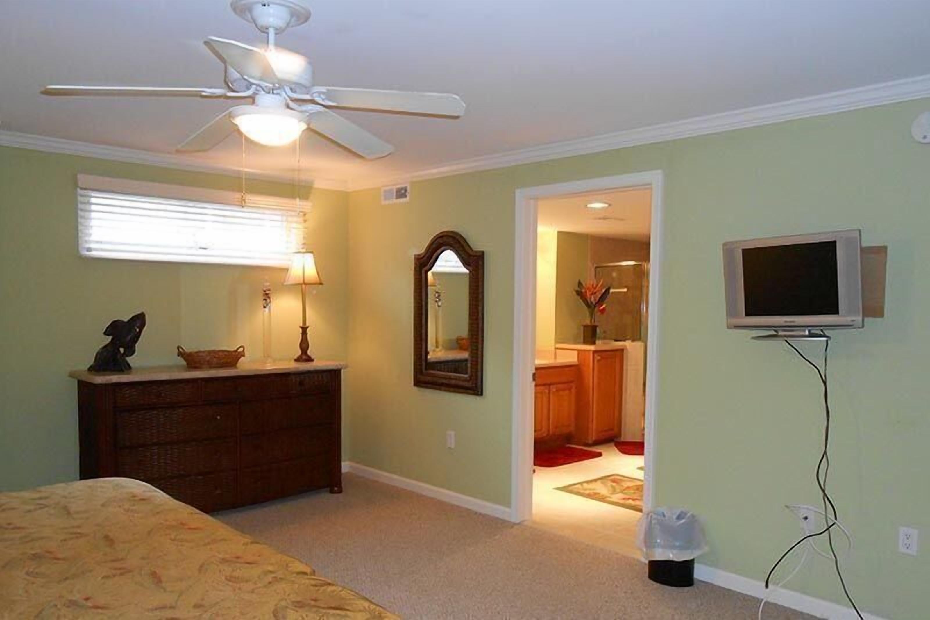 Ein Schlafzimmer mit Bett, Kommode, Deckenventilator und einem an der Wand montierten Fernseher.