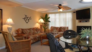 A living room with a sofa, chairs, a coffee table, a TV, and a ceiling fan. - Bel Mare 100 4 Bedroom Condo by RedAwning (Ocean City)