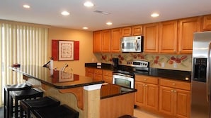 A modern kitchen with wooden cabinets, a stainless steel refrigerator, a microwave, and a stove. - Bel Mare 100 4 Bedroom Condo by RedAwning (Ocean City)