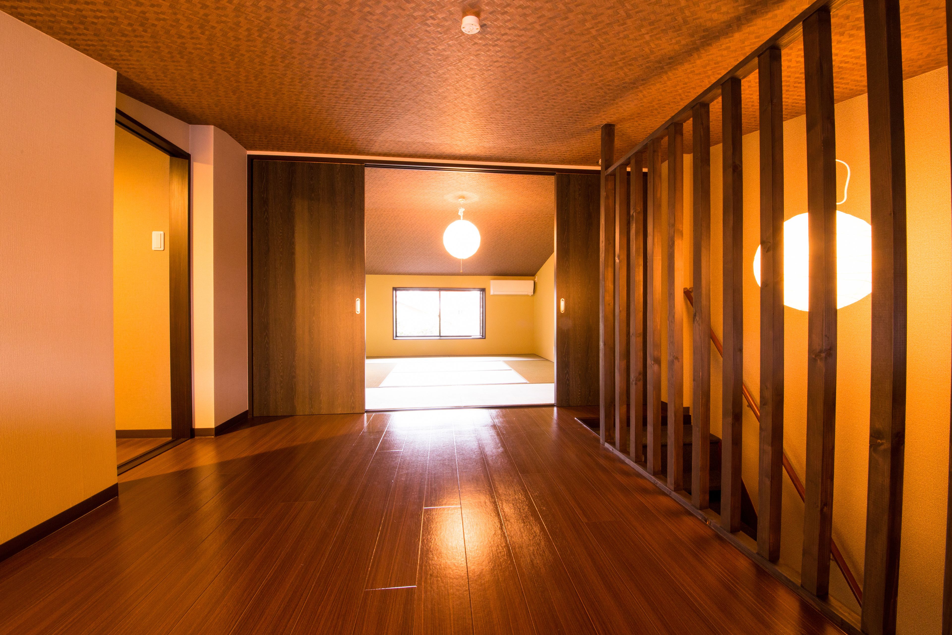 A hallway with wooden flooring, a ceiling fan, and a view of a room with a window.