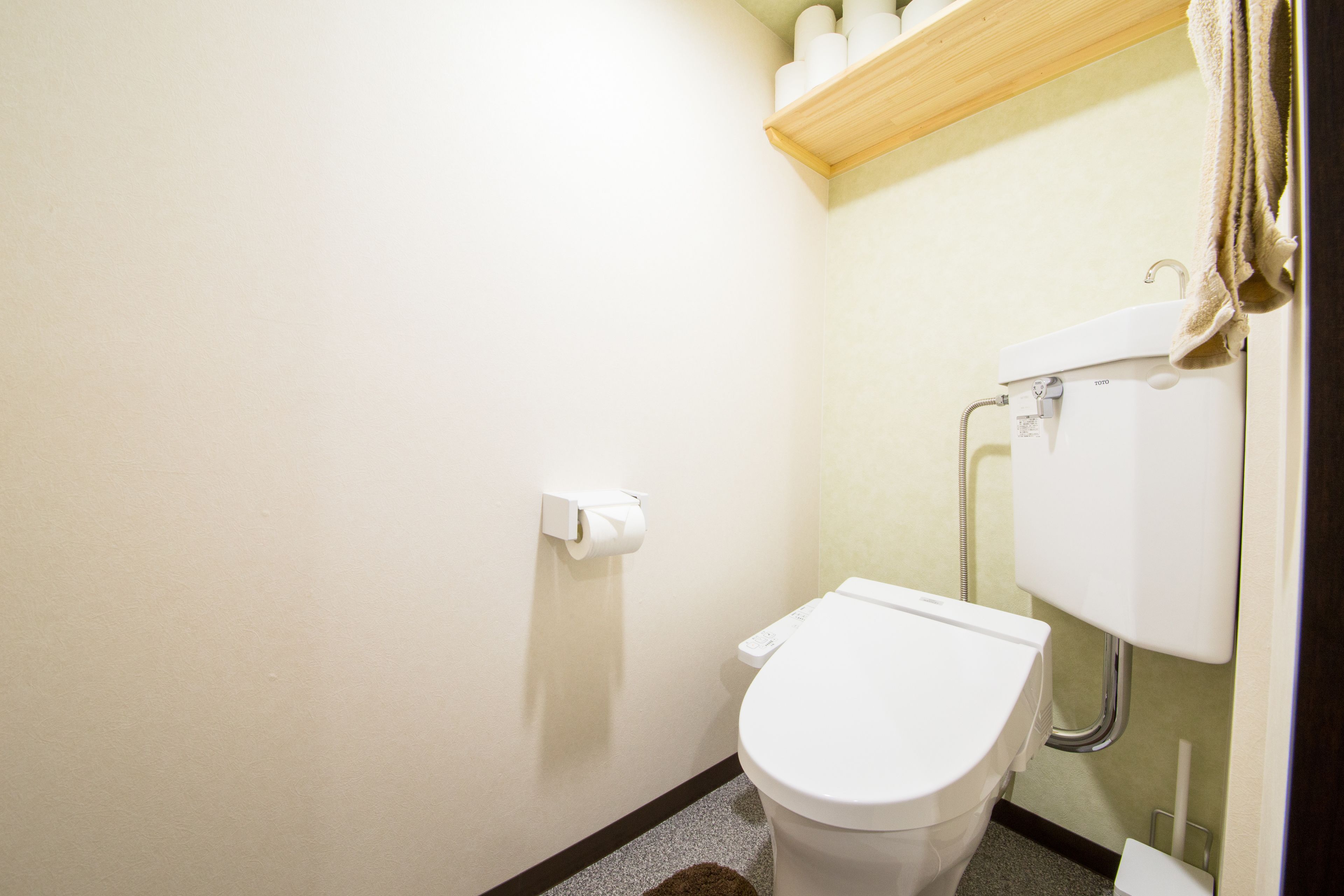 A small, clean bathroom with a toilet, a shelf with toiletries, and a towel hanging on a hook.