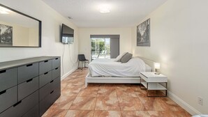 A bedroom with a bed, bedside table, lamp, dresser, and a large window. - North Timucuan Trail 1208 3 Bedroom Villa by RedAwning (Inverness)