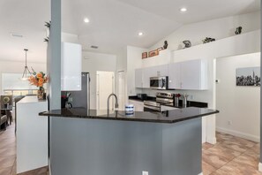 A modern kitchen with a central island, stainless steel appliances, and a dining area with a glass table. - North Timucuan Trail 1208 3 Bedroom Villa by RedAwning (Inverness)
