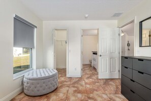 A hallway with a grey ottoman, a white door, and a tiled floor.
