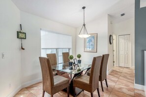A dining area with a glass table and four chairs, a ceiling light, a framed picture on the wall, and a door in the background. - North Timucuan Trail 1208 3 Bedroom Villa by RedAwning (Inverness)