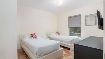 A hotel room with two beds, a small bedside table, a window with a view, and a TV mounted on the wall.