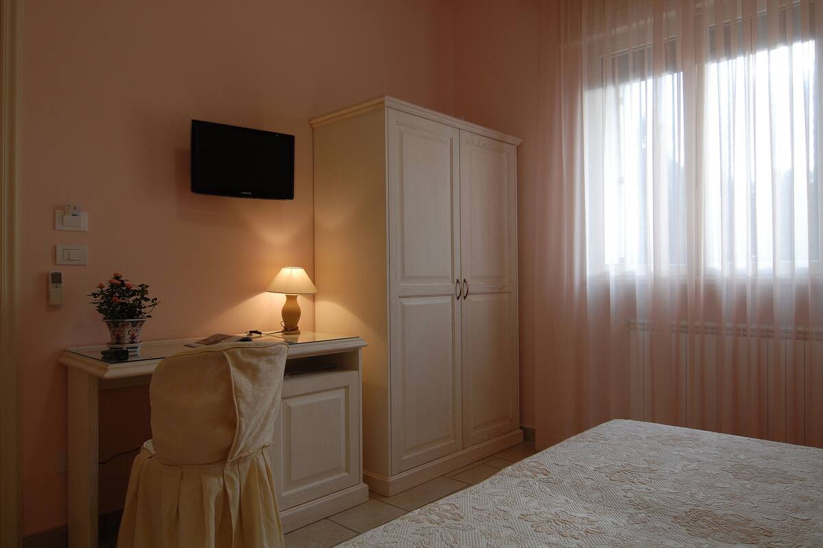 Ein Schlafzimmer mit einem Bett, einem Schreibtisch mit Lampe, einem Fernseher und einem Kleiderschrank.