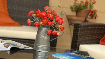 A metal vase with red flowers on a glass table, a magazine, and a blue book.