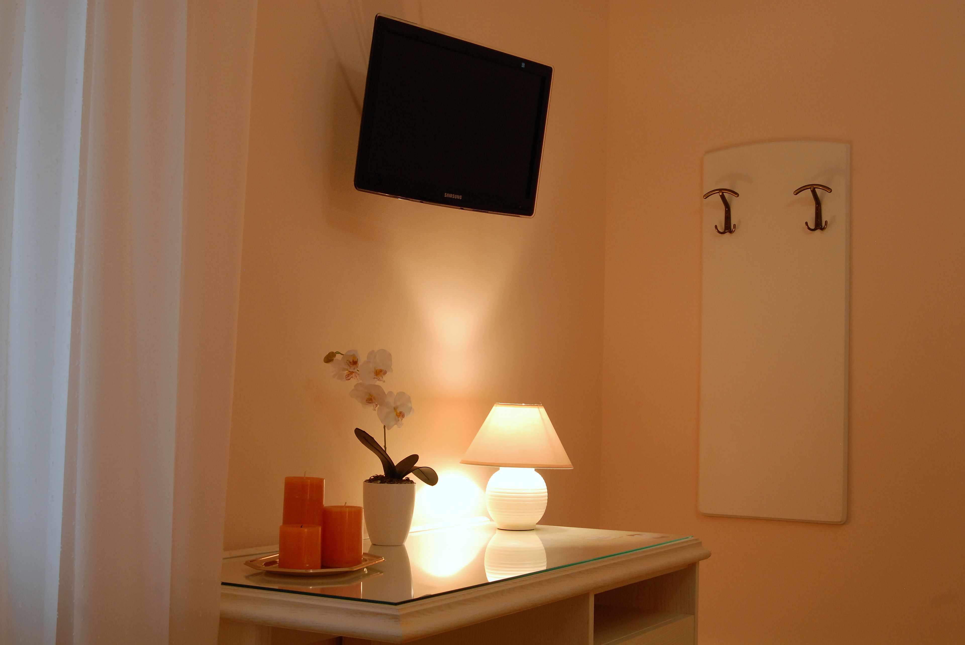 Et værelse med et fladskærms-tv monteret på væggen, et lille bord med lampe, stearinlys og en orkidé.