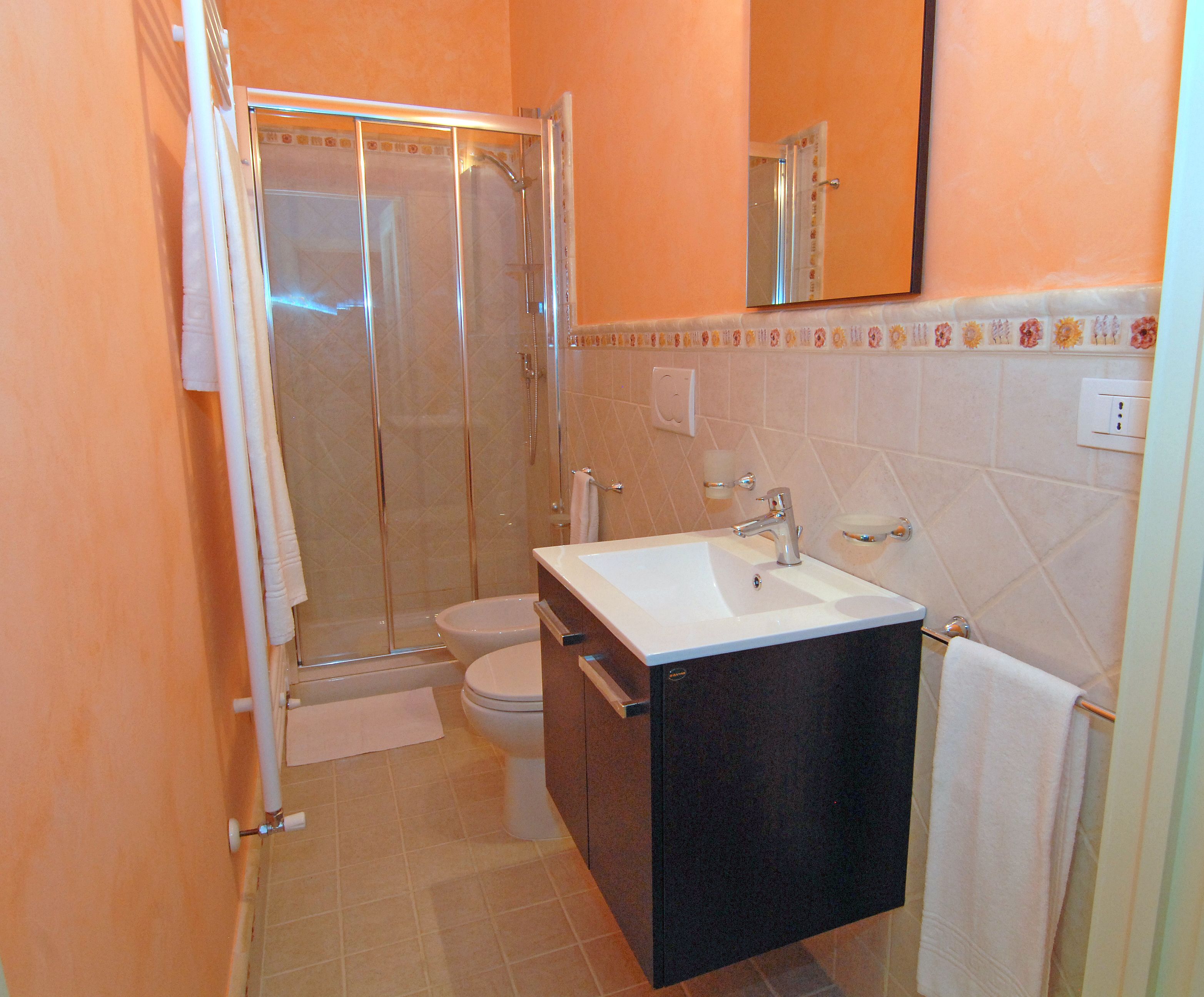 Een badkamer met een glazen douchecabine, een wit toilet, een wastafel met spiegel erboven en een handdoekhouder.