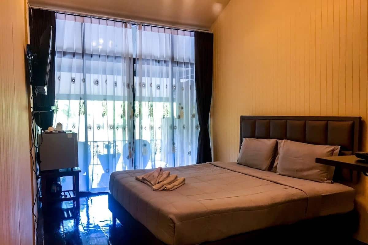 A bedroom with a bed, a nightstand, a chair, and a window with sheer curtains.