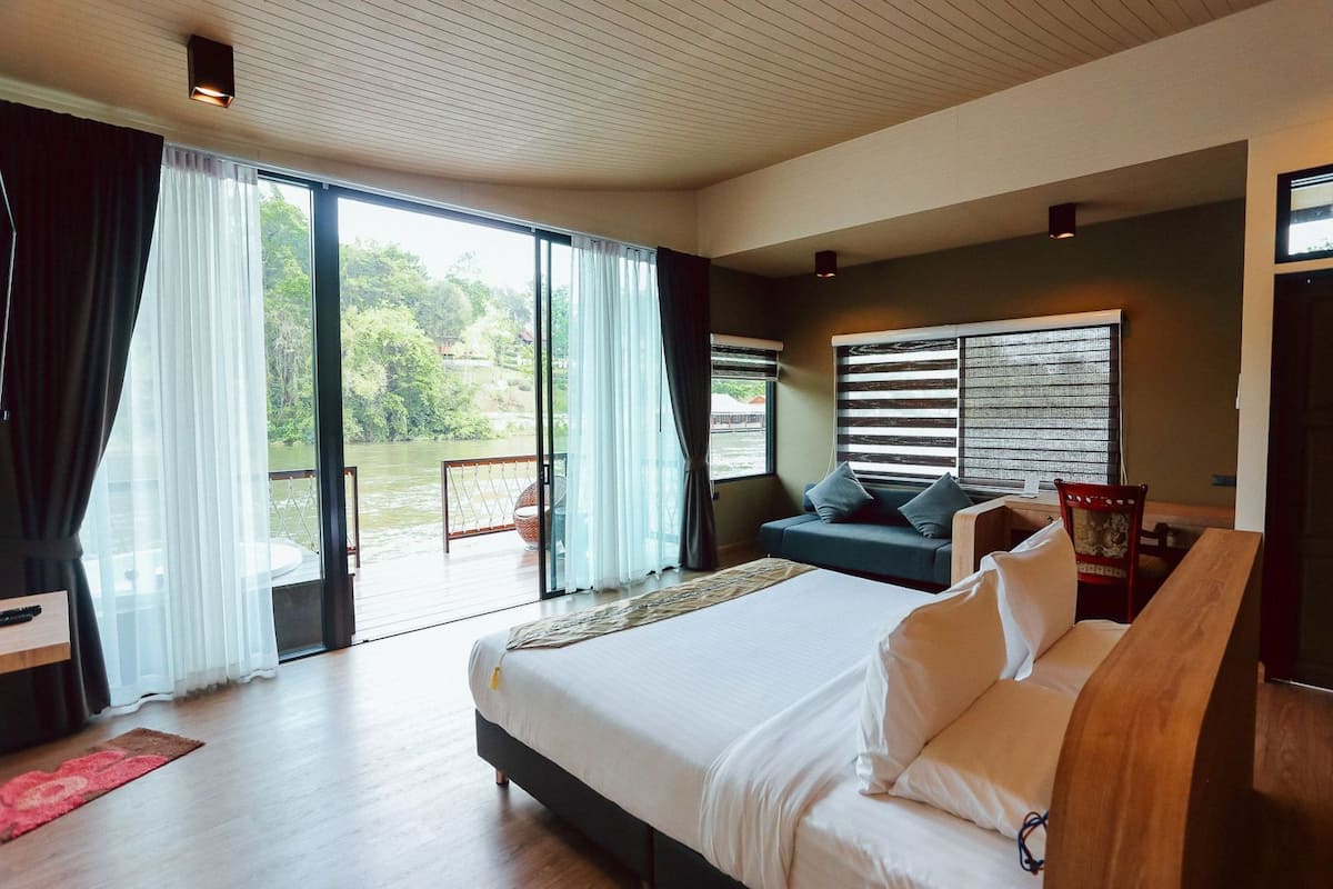 A bedroom with a large bed, a sofa, a desk, and a view of a water body.