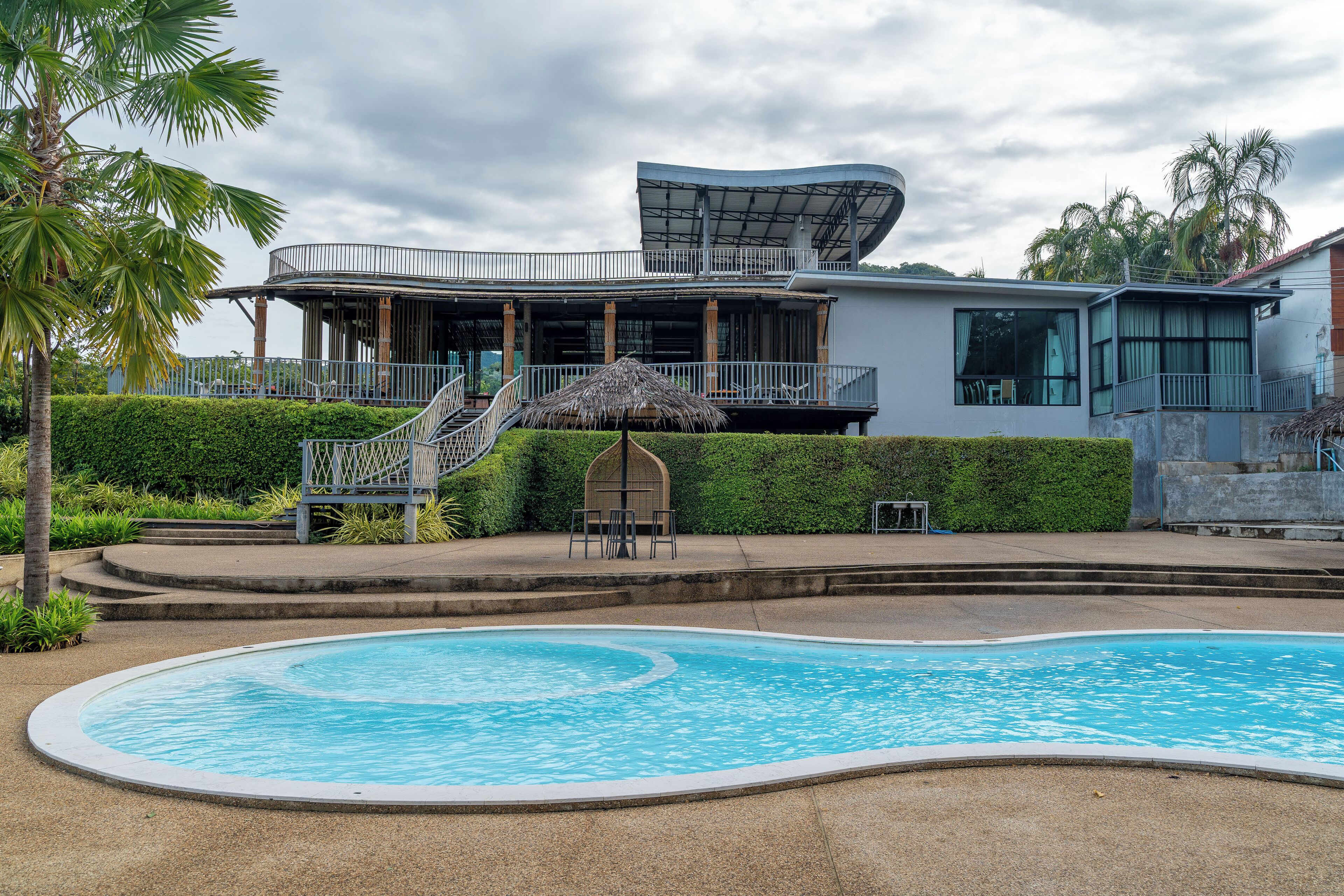 A modern building with a pool, a covered outdoor area, and a staircase leading to a balcony.