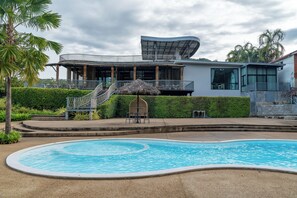 A modern building with a pool, a covered outdoor area, and a staircase leading to a balcony. - Binlha Raft Resort (Sai Yok)