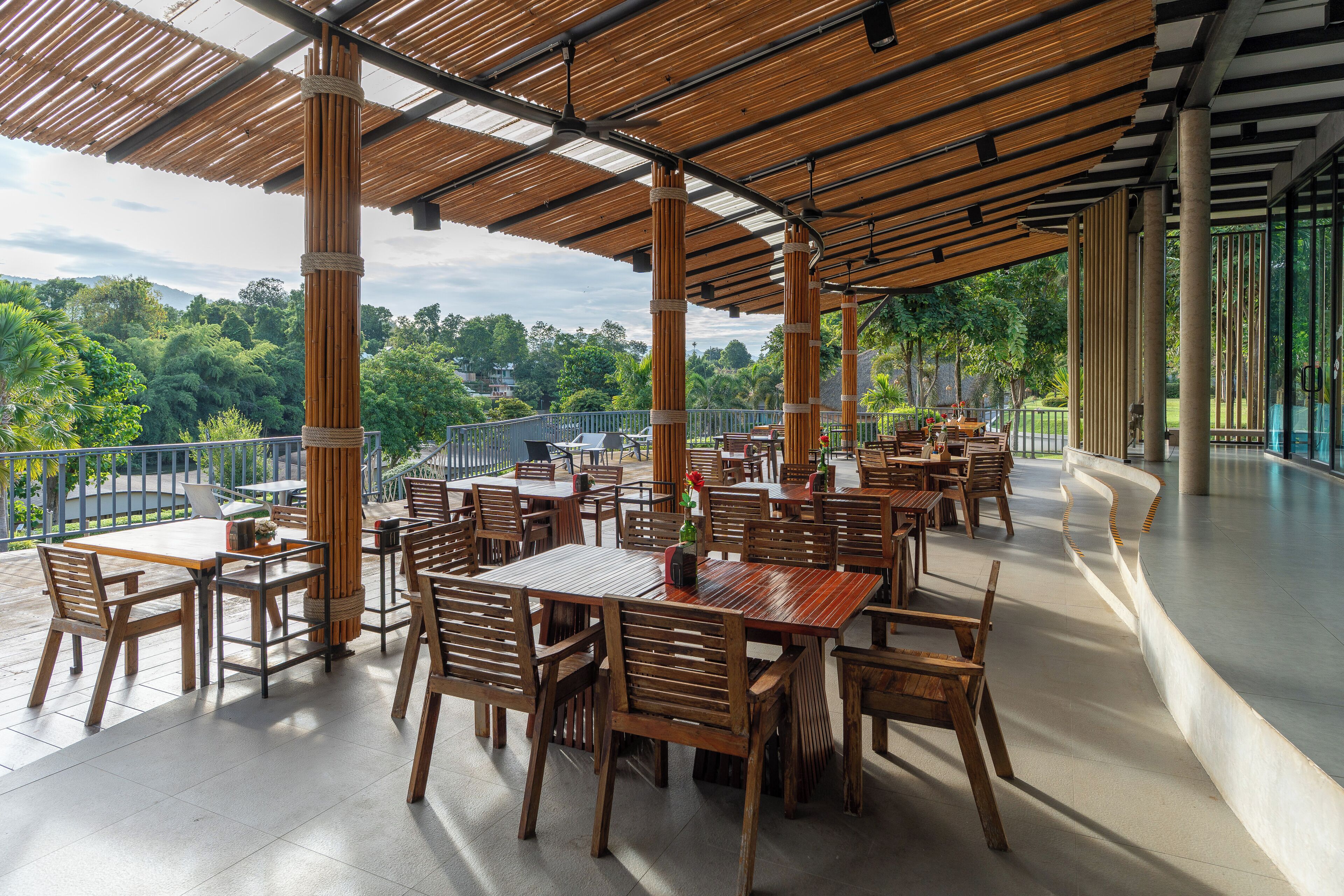 An outdoor dining area with wooden tables and chairs, surrounded by a covered roof structure.