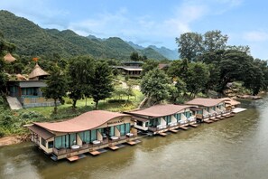 Un hotel junto al río con alojamientos flotantes, una piscina y montañas al fondo.
