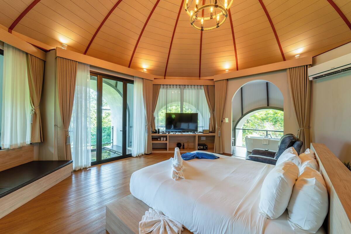 A spacious bedroom with a large bed, a television, and a sliding glass door leading to an outdoor area.