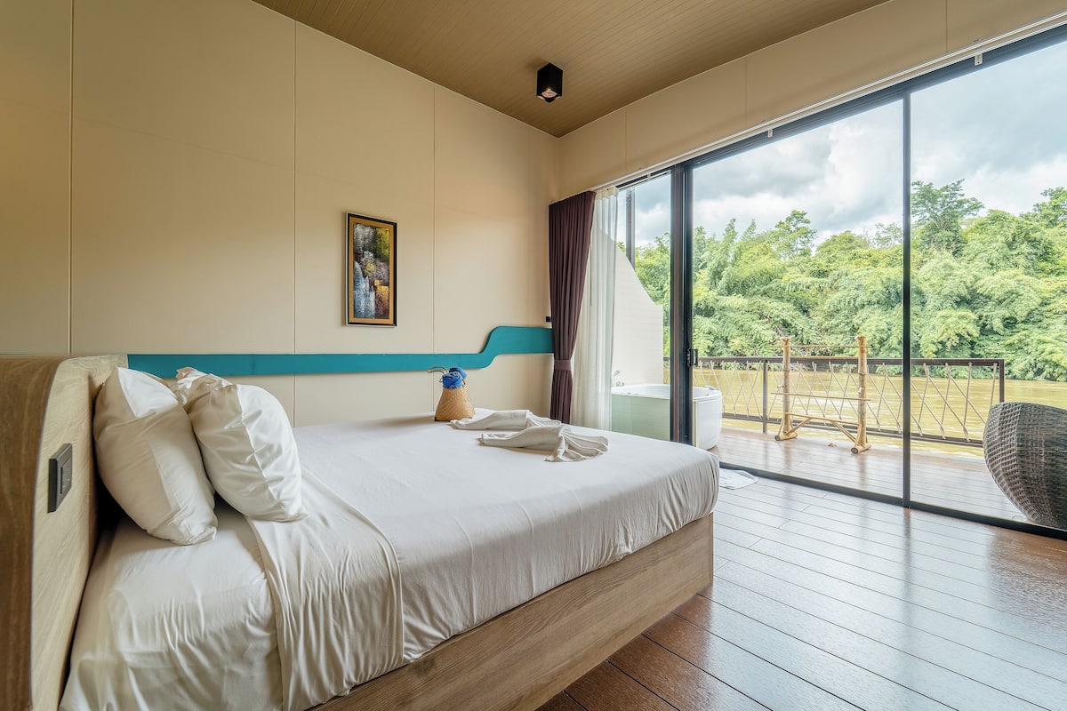 A bedroom with a large bed, a painting on the wall, and a view of the outdoors through a sliding door.