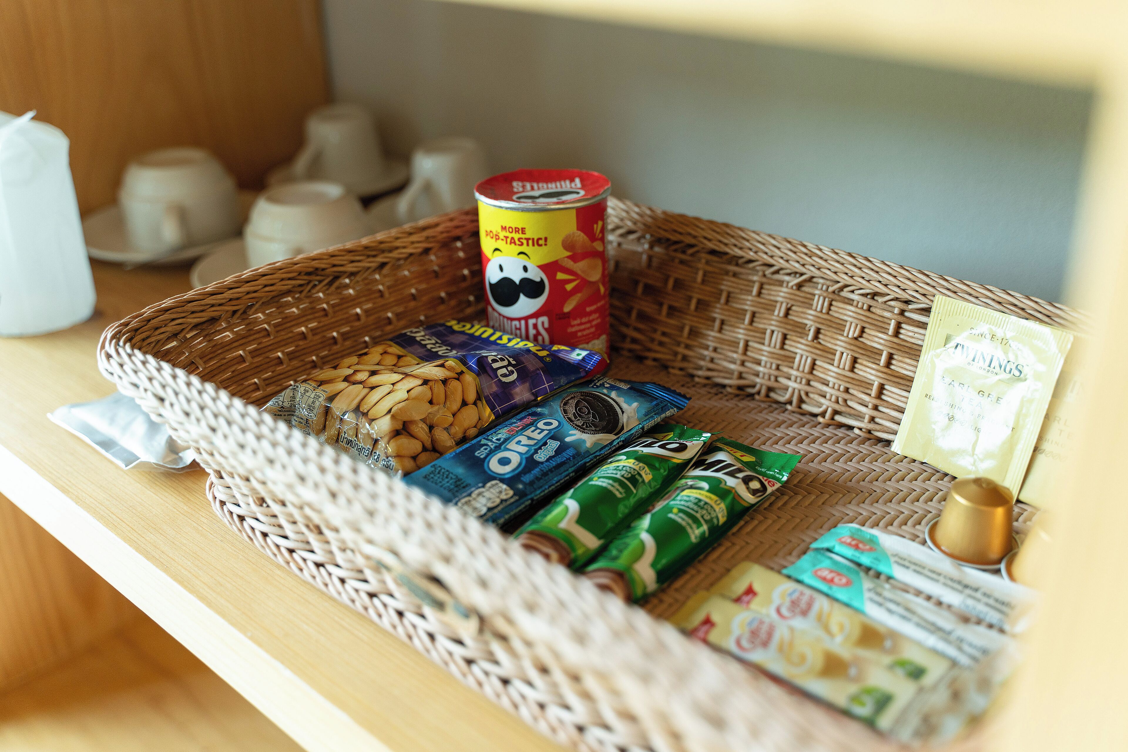 A wicker basket containing snacks, a can of Pringles, and various packaged foods on a wooden surface.