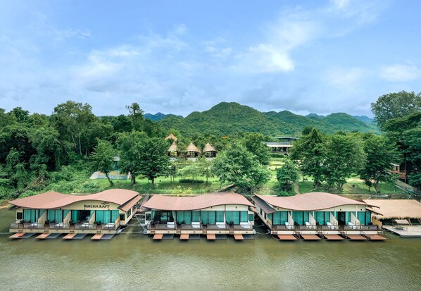 A riverside hotel with floating bungalows, a swimming pool, and a view of the surrounding mountains. - Binlha Raft Resort (Sai Yok)