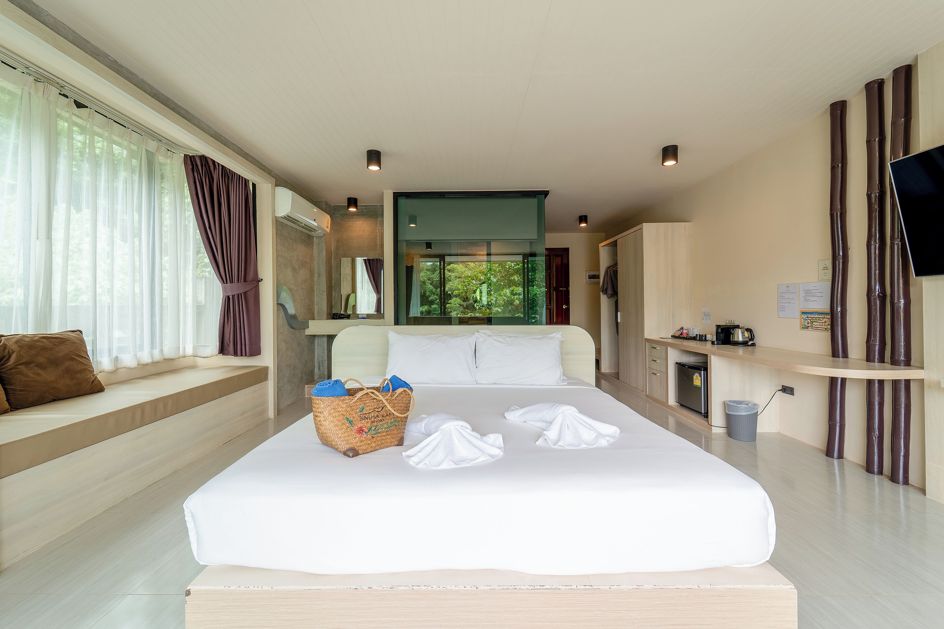 Una habitación de hotel moderna con una cama grande, un área de descanso con vistas, una kitchenette pequeña y un televisor en la pared.