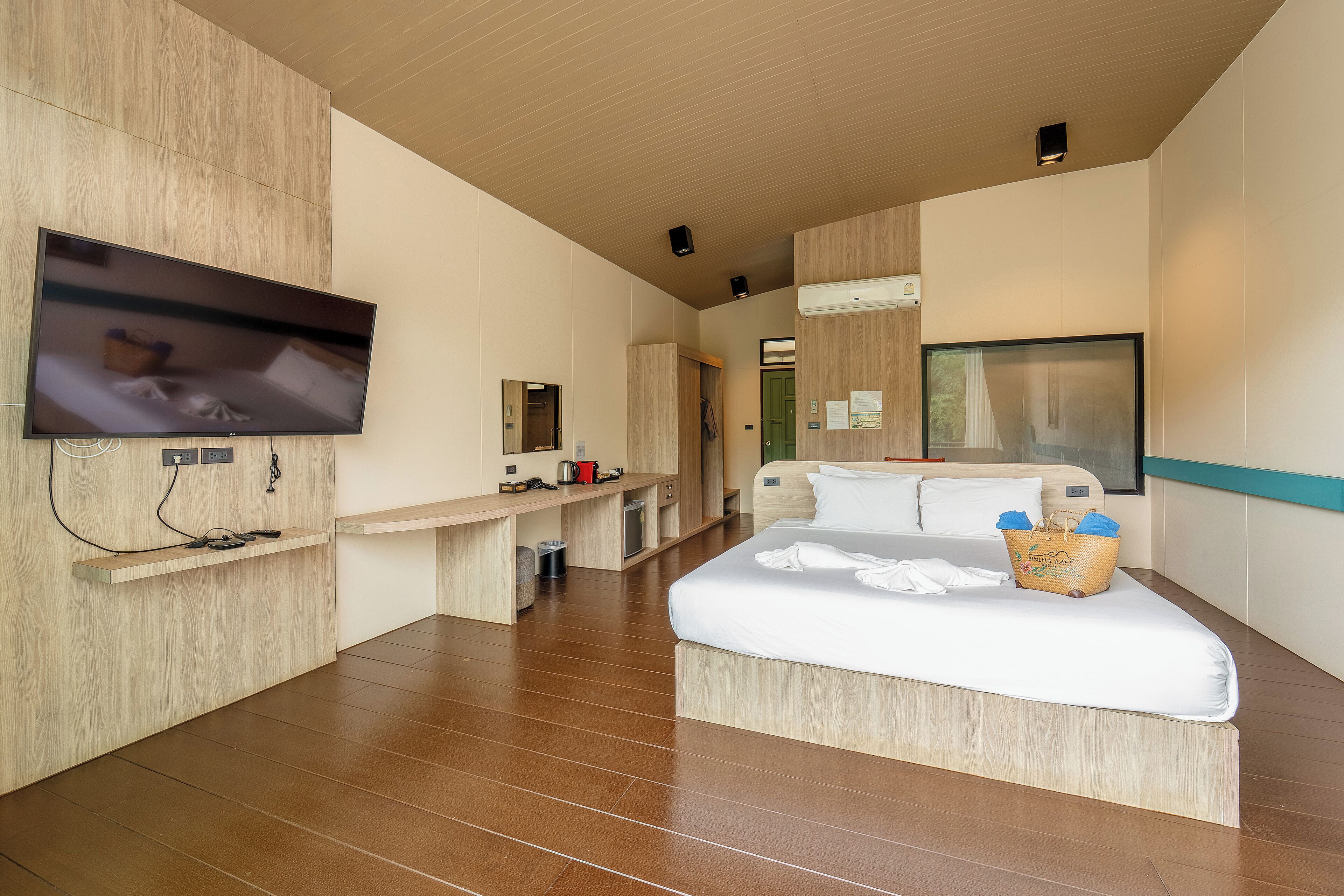 Ein modernes Hotelzimmer mit Flachbildfernseher, einem Bett mit Korb, einem Schreibtisch und einem Kleiderschrank.