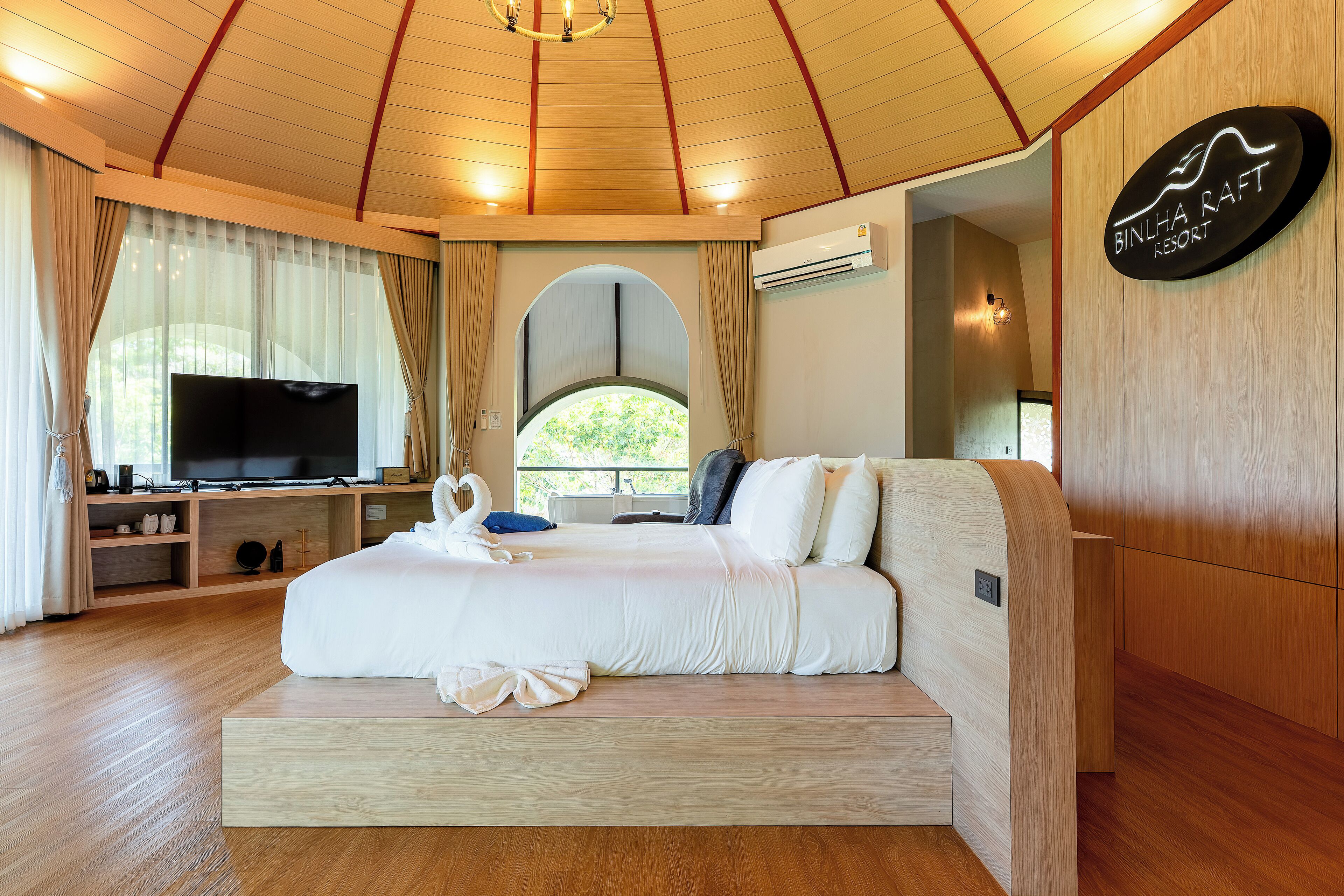 Une chambre d’hôtel moderne avec un grand lit, une télévision et une vue sur la verdure par la fenêtre.