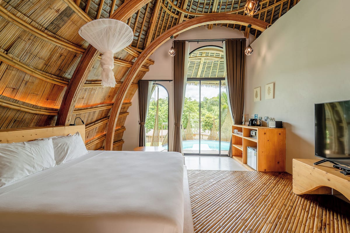 A room with a bed, a TV, a wooden desk, and a view of a swimming pool.